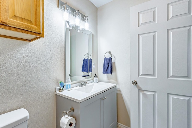 bathroom featuring a textured wall, vanity, and toilet