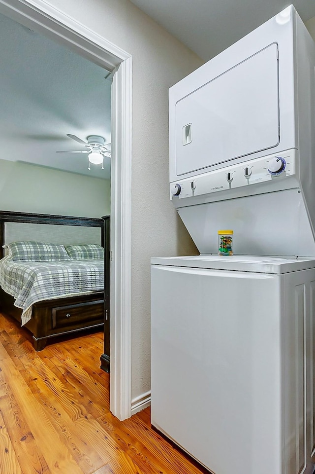 laundry room with light wood finished floors, ceiling fan, laundry area, and stacked washer / dryer