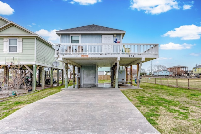 beach home with a carport, concrete driveway, roof with shingles, and a front yard