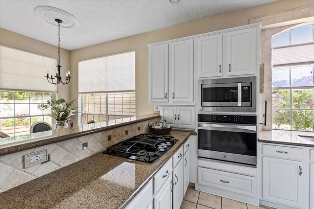 kitchen with white cabinets, stainless steel appliances, an inviting chandelier, and a healthy amount of sunlight