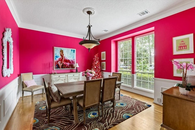 dining space with wainscoting, wood finished floors, and crown molding