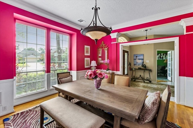 dining space with light wood-type flooring, crown molding, and a textured ceiling