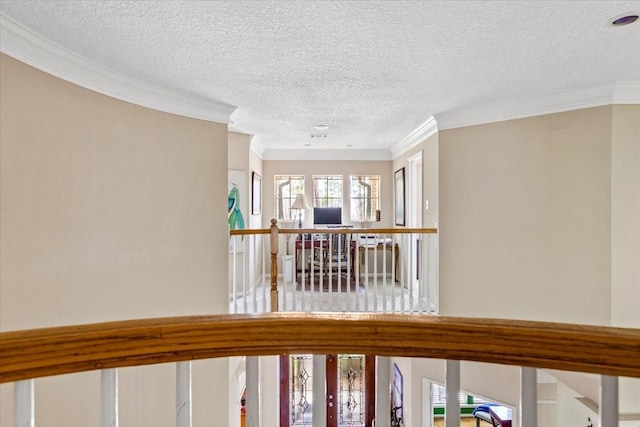 hall with a textured ceiling, ornamental molding, and an upstairs landing