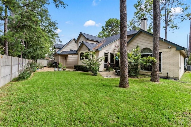 back of property with a fenced backyard, a chimney, a lawn, and brick siding