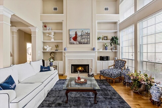 living room with built in features, hardwood / wood-style floors, ornate columns, and a high ceiling