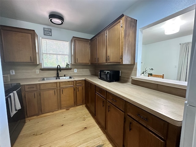 kitchen featuring sink, light wood-type flooring, backsplash, and stove