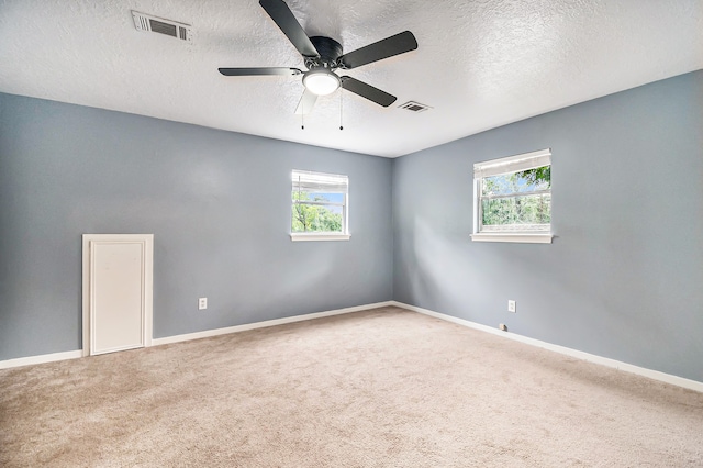 unfurnished room featuring a textured ceiling, carpet, a wealth of natural light, and ceiling fan