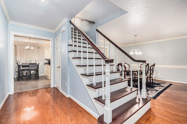 staircase with ornamental molding, wood-type flooring, a textured ceiling, and a chandelier