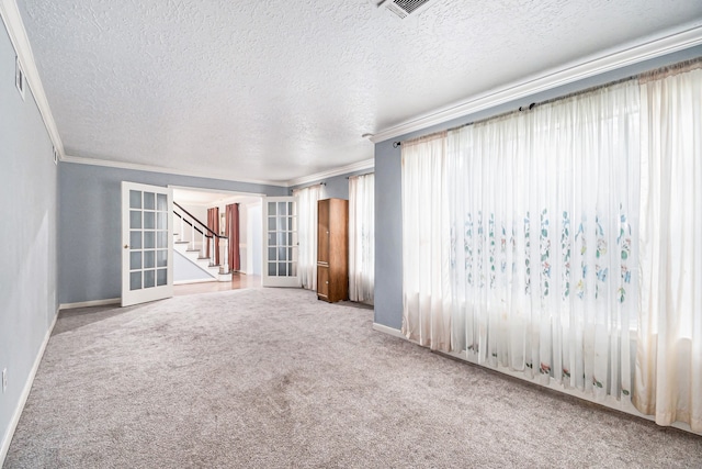 empty room featuring a textured ceiling, french doors, carpet floors, and ornamental molding