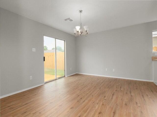 empty room with a notable chandelier and light hardwood / wood-style floors