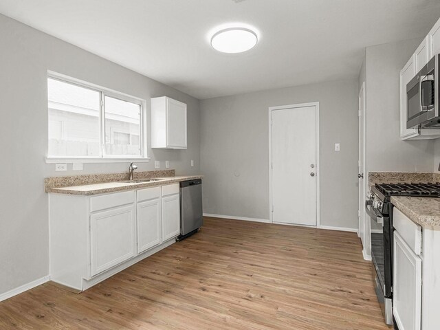 kitchen with white cabinets, appliances with stainless steel finishes, sink, and light hardwood / wood-style flooring