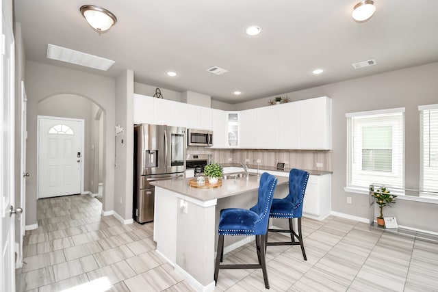 kitchen featuring stainless steel appliances, a center island with sink, a breakfast bar, light tile patterned floors, and backsplash