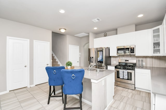 kitchen featuring white cabinetry, tasteful backsplash, stainless steel appliances, an island with sink, and light tile patterned floors