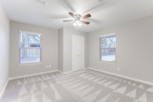 empty room featuring ceiling fan, a healthy amount of sunlight, and light colored carpet