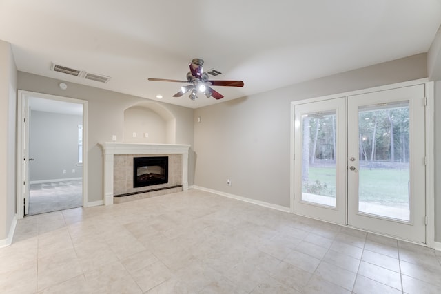 unfurnished living room with french doors, a tile fireplace, light tile patterned floors, and ceiling fan