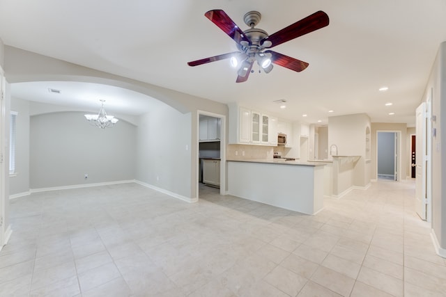 kitchen with kitchen peninsula, light tile patterned floors, decorative backsplash, ceiling fan with notable chandelier, and white cabinetry