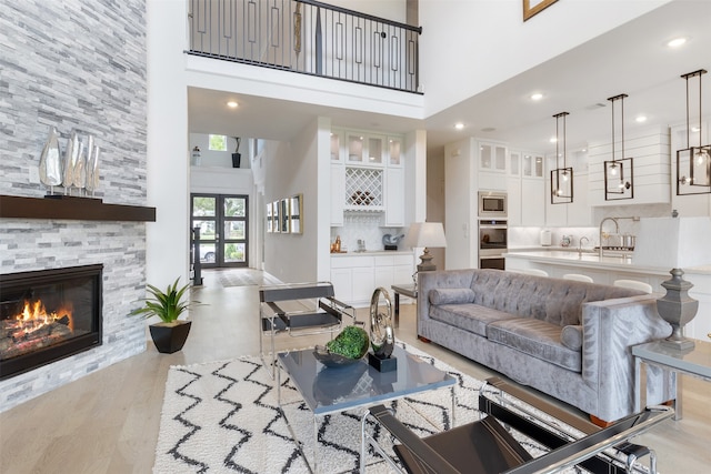 living room featuring a fireplace, a towering ceiling, light hardwood / wood-style floors, and sink