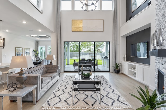 living room featuring an inviting chandelier, a stone fireplace, light hardwood / wood-style floors, and a towering ceiling