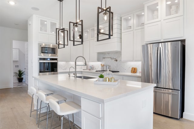 kitchen with light hardwood / wood-style floors, appliances with stainless steel finishes, tasteful backsplash, and a center island with sink