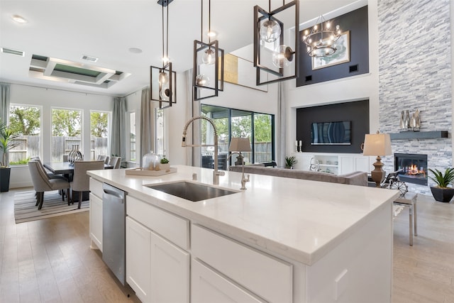 kitchen with a stone fireplace, pendant lighting, light wood-type flooring, and an island with sink