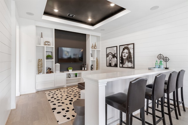 bar with white cabinetry, light wood-type flooring, built in shelves, and a raised ceiling