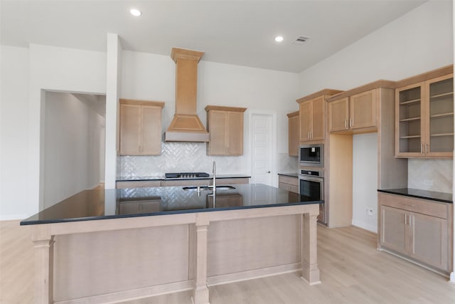 kitchen with appliances with stainless steel finishes, sink, custom exhaust hood, a kitchen island with sink, and light hardwood / wood-style floors