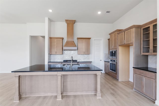 kitchen featuring custom exhaust hood, an island with sink, decorative backsplash, and stainless steel appliances