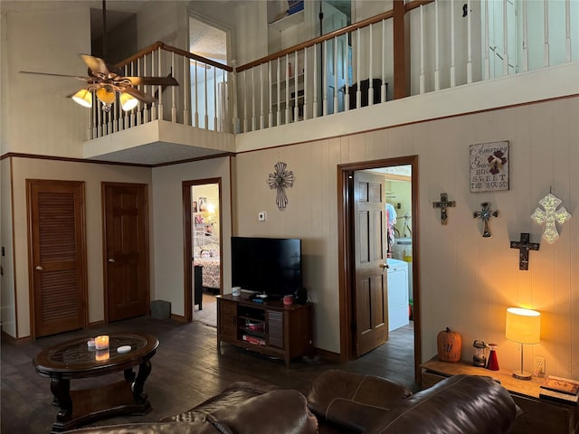 living room featuring ceiling fan, a high ceiling, dark hardwood / wood-style floors, and washer / dryer