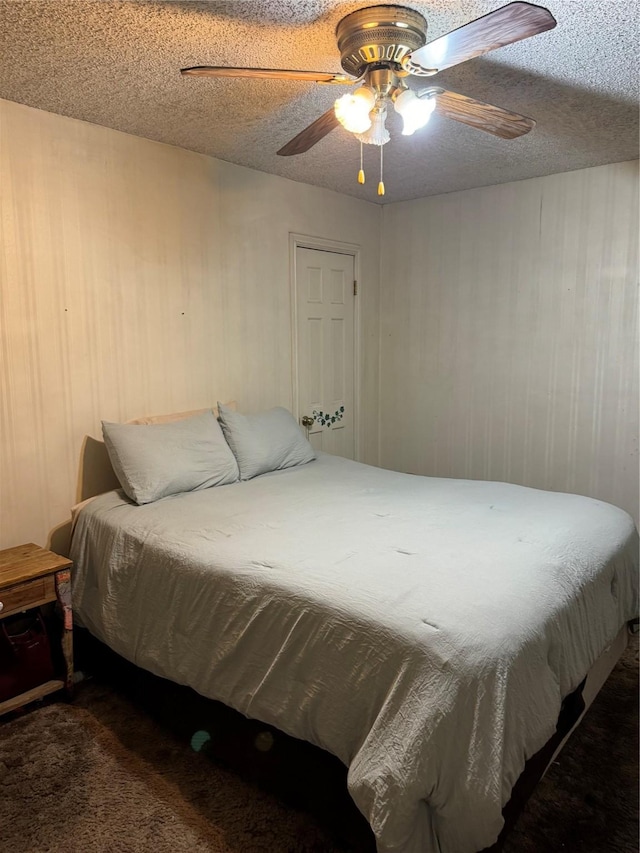 bedroom with ceiling fan, dark carpet, a textured ceiling, and wood walls