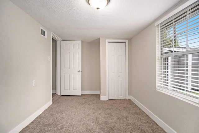 unfurnished bedroom featuring light carpet, a textured ceiling, and a closet