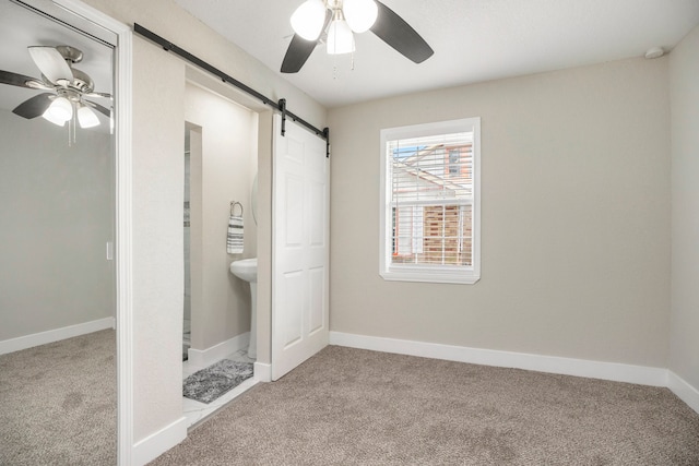 unfurnished bedroom featuring a barn door, ceiling fan, ensuite bath, and carpet