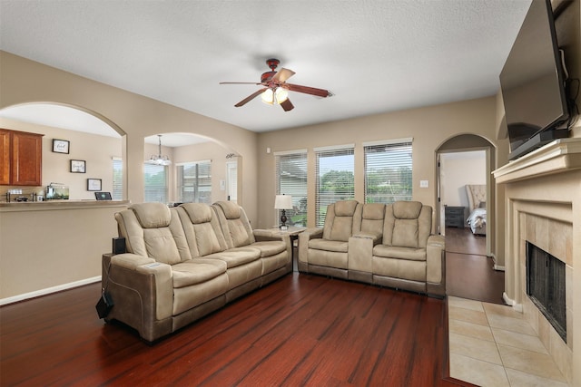 living room featuring ceiling fan with notable chandelier, light hardwood / wood-style floors, a premium fireplace, and a textured ceiling