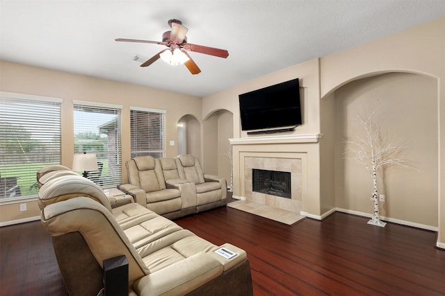 living room featuring ceiling fan, dark hardwood / wood-style flooring, and a tiled fireplace