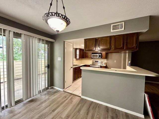 kitchen featuring light tile patterned floors, a textured ceiling, kitchen peninsula, appliances with stainless steel finishes, and dark brown cabinetry