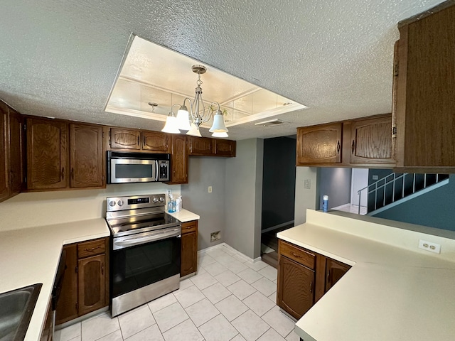 kitchen featuring a chandelier, a textured ceiling, a tray ceiling, hanging light fixtures, and appliances with stainless steel finishes