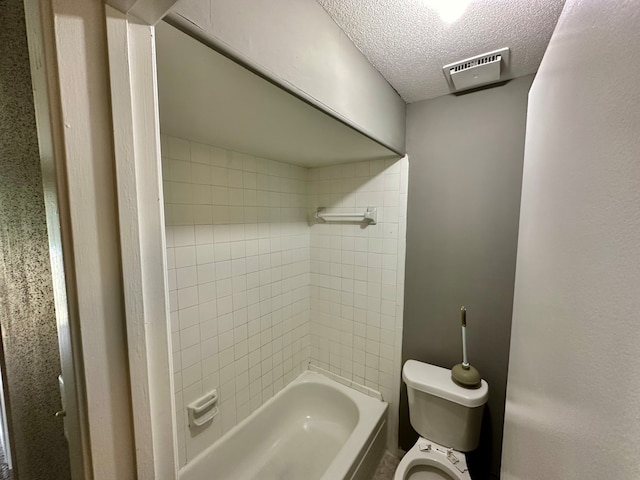 bathroom with tiled shower / bath combo, toilet, and a textured ceiling