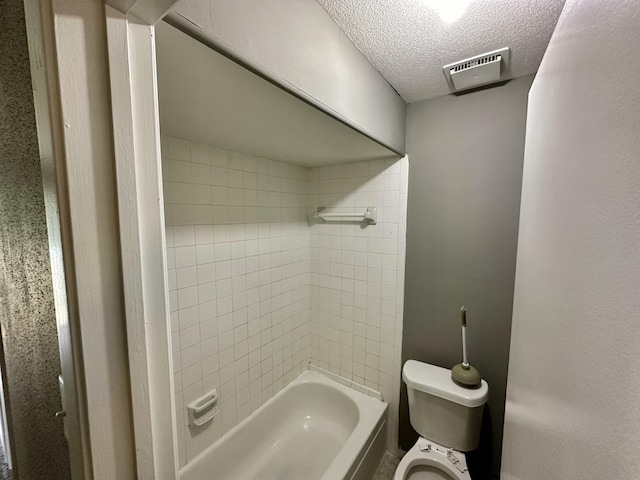 bathroom featuring a textured ceiling, toilet, and tiled shower / bath combo