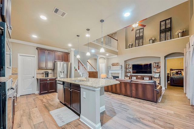 kitchen featuring stainless steel appliances, sink, a fireplace, an island with sink, and ceiling fan