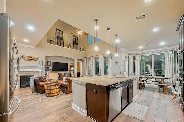 kitchen with dark brown cabinets, a center island with sink, stainless steel appliances, a tile fireplace, and sink