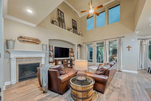 living room featuring a tiled fireplace, ornamental molding, light wood-type flooring, and ceiling fan