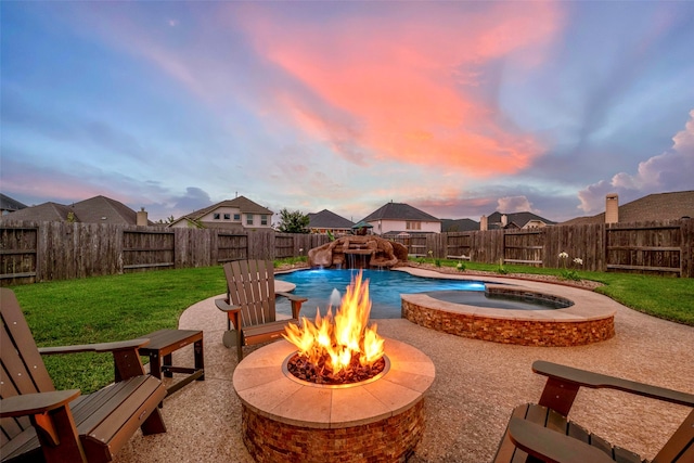 pool at dusk featuring pool water feature, an in ground hot tub, a lawn, a fire pit, and a patio