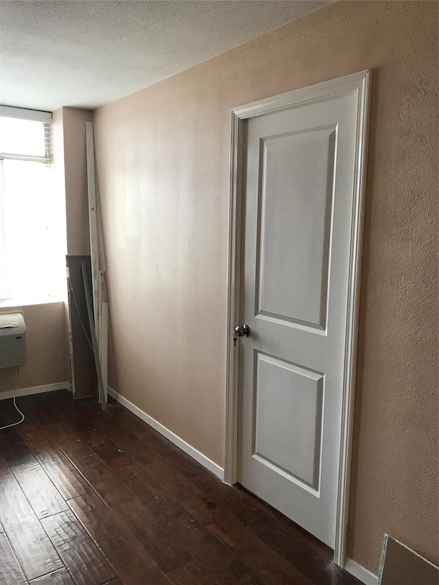 empty room featuring dark wood-type flooring, a wall mounted AC, and a textured ceiling