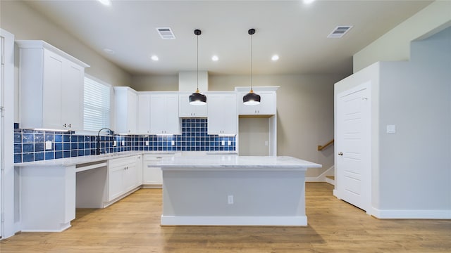 kitchen featuring sink, a kitchen island, white cabinetry, light hardwood / wood-style floors, and pendant lighting