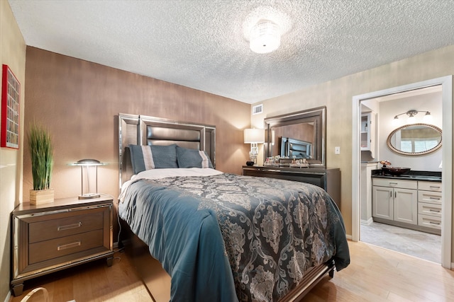 bedroom with light hardwood / wood-style floors, a textured ceiling, and connected bathroom