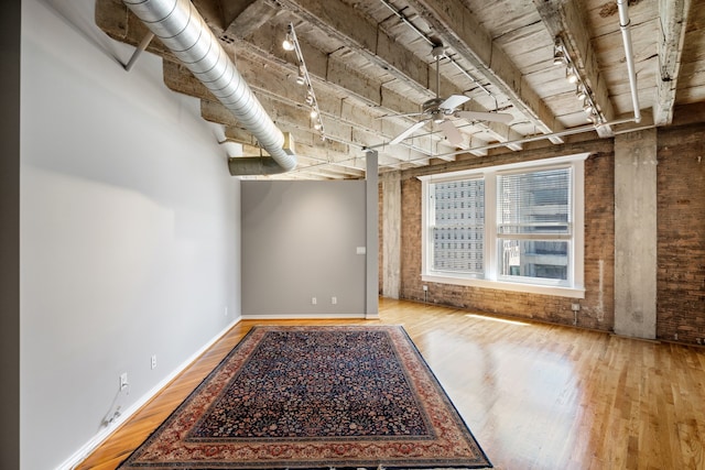 empty room with hardwood / wood-style flooring, brick wall, and ceiling fan