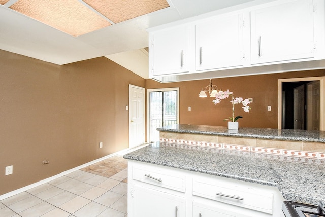 kitchen featuring an inviting chandelier, light tile patterned floors, light stone countertops, lofted ceiling, and white cabinetry