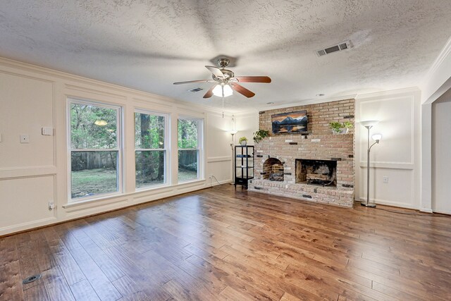 unfurnished living room with a textured ceiling, ornamental molding, hardwood / wood-style flooring, and a brick fireplace