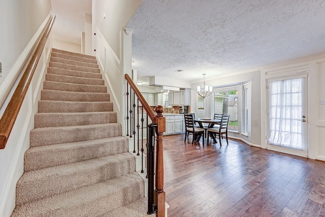 staircase with a textured ceiling, a notable chandelier, dark wood-type flooring, and crown molding