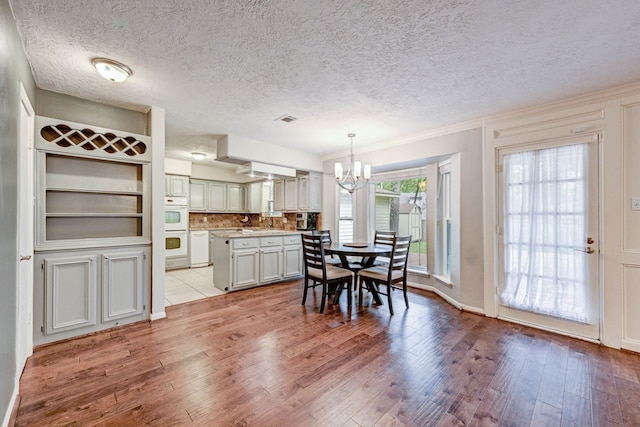 dining area featuring a textured ceiling, built in shelves, a chandelier, and light hardwood / wood-style floors