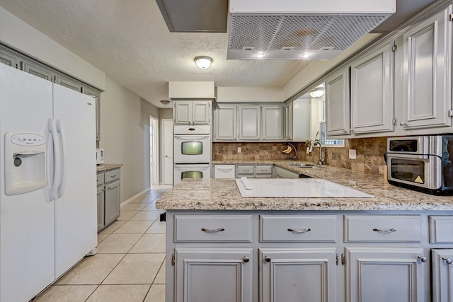 kitchen with decorative backsplash, wall chimney range hood, gray cabinetry, white appliances, and sink